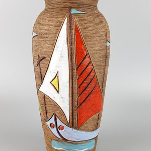Puede incluir: Un jarr&oacute;n de cer&aacute;mica marr&oacute;n con un dise&ntilde;o de velero estilizado. El velero est&aacute; pintado en blanco, rojo, azul y amarillo. El jarr&oacute;n tiene una superficie texturizada.