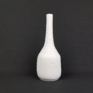 May include: White ceramic vase with a textured, raised design. The vase has a tall, slender neck and a rounded base.