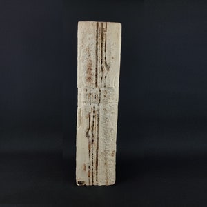 Puede incluir: Una escultura de cerámica blanca con una superficie texturizada y líneas marrones que corren verticalmente. La escultura es rectangular y tiene un aspecto áspero y sin terminar.