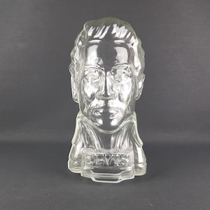 May include: A clear glass bust of a man's head and shoulders. The bust is a vintage glass bottle with the word "DEWYS" etched on the front.