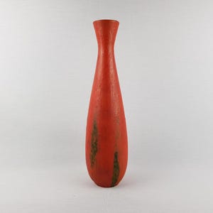 Puede incluir: Un jarrón rojo alto con una superficie texturizada. El jarrón tiene una forma delgada y alargada con una parte superior acampanada. Parches marrones oscuros añaden un toque de contraste al rojo. Este jarrón decorativo es adecuado para la decoración del hogar.