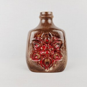 Peut inclure: Un vase en céramique marron avec un motif floral rouge. Le vase a une forme rectangulaire aux bords arrondis et un col étroit. Le motif rouge est en relief et texturé, ajoutant un intérêt visuel à la pièce.