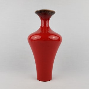 May include: A vibrant red vase with a glossy finish, featuring a flared base and a slender neck. The rim is a dark brown. The vase, with its smooth surface, stands out against a plain white backdrop.