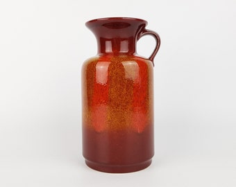 Könnte beinhalten: Eine rote und orangefarbene Keramikvase mit brauner Glasur. Die Vase hat eine breite Öffnung und einen Henkel an einer Seite.