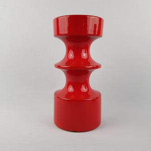 Könnte beinhalten: Eine leuchtend rote Keramikvase mit glänzendem Finish. Die Vase hat eine einzigartige Sanduhrform mit breitem Boden und Oberteil sowie einem schmaleren Mittelteil. Die Gesamthöhe beträgt ca. 25 cm.