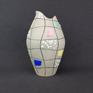 May include: A gray ceramic vase with a geometric design. The vase is decorated with black lines, white dots, and colorful squares in shades of blue, green, yellow, and pink.