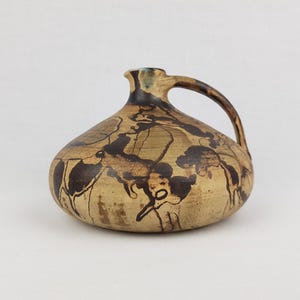 Könnte beinhalten: Eine braune Keramikvase mit einem breiten, abgerundeten Körper und einem einzigen Henkel. Die Vase ist mit einem braunen und schwarzen abstrakten Muster verziert.