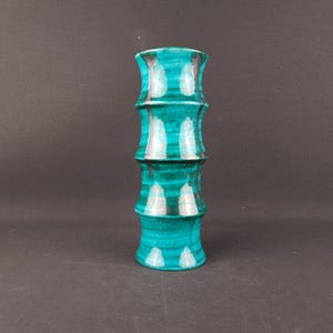 Op de afbeelding: Een turquoise keramische vaas met een bamboe-achtig ontwerp. De vaas is ongeveer 25 cm hoog en heeft een reeks gestapelde, cilindrische secties. Witte accenten benadrukken de ribbels en de vaas heeft een glanzende afwerking.