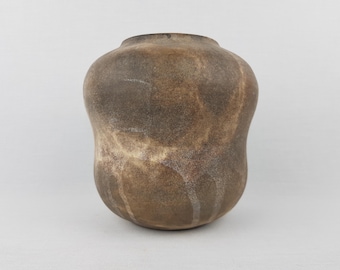 May include: A brown ceramic vase with a rounded body and a narrow neck. The vase has a textured surface with a mottled appearance, featuring shades of brown and tan. The vase is approximately 10 inches tall.