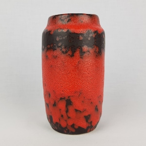 Puede incluir: Un jarrón cilíndrico de cerámica con una superficie texturizada y moteada. El jarrón es principalmente rojo con una banda marrón oscuro cerca de la parte superior y detalles en marrón oscuro en la base. El jarrón tiene una abertura ancha.