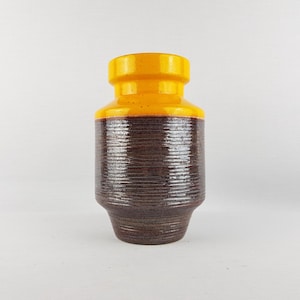 May include: A ceramic vase with a cylindrical body and a flared base. The top section is a bright yellow, while the middle section is a dark brown with a textured, horizontal pattern. The vase is a decorative item.