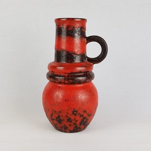 May include: A red and black ceramic vase with a rounded body and a tall, cylindrical neck. The vase has a single handle and a speckled glaze.