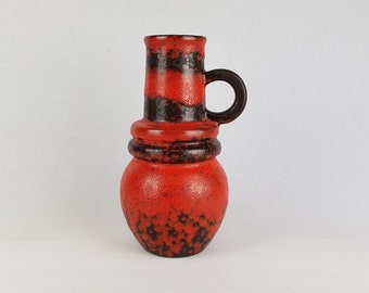 May include: A red and black ceramic vase with a rounded body and a tall, cylindrical neck. The vase has a single handle and a speckled glaze.