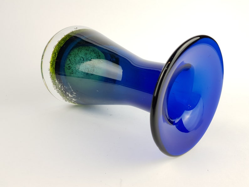 May include: A blue glass vase with a flared base and a green glass accent at the top.