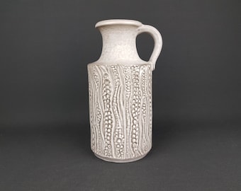 May include: A white ceramic vase with a textured design of wavy lines and small circles. The vase has a wide mouth and a handle.