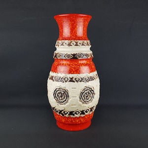 Puede incluir: Un jarrón de cerámica rojo y blanco con un patrón geométrico. El jarrón tiene una base ancha y un cuello estrecho.