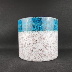 May include: A cylindrical ceramic planter featuring a two-tone design. The upper section displays a vibrant, textured turquoise blue glaze, while the lower portion is finished in a white glaze with a speckled, reddish-brown mottled pattern.