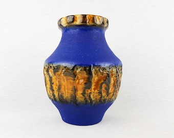 May include: A cobalt blue ceramic vase with a textured, earthy design in shades of brown and black. The rim has a textured, dark brown and tan pattern. A decorative piece for home decor.
