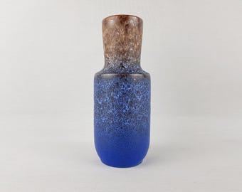 Könnte beinhalten: Eine hohe Keramikvase mit Farbverlauf. Der obere Teil ist braun, geht in ein gesprenkeltes Blau und dann in einen einfarbigen blauen Sockel über. Die Vase hat einen schmalen Hals und einen breiteren Körper.