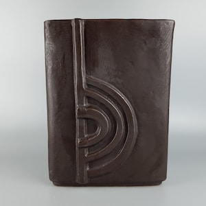 Puede incluir: Un jarrón de cerámica marrón oscuro con un diseño geométrico. El jarrón tiene una forma rectangular y un diseño en relieve en la parte delantera.