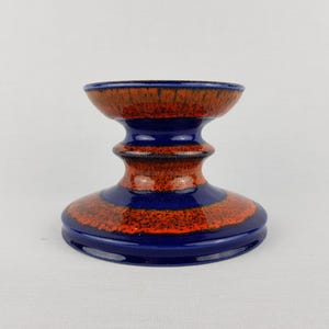 May include: A blue and orange ceramic candle holder with a wide base and a narrow middle section. The holder has a textured, speckled finish.