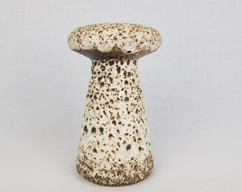 May include: A white ceramic vase with a brown speckled glaze, shaped like a mushroom. The vase has a wide, rounded top and a narrow base.