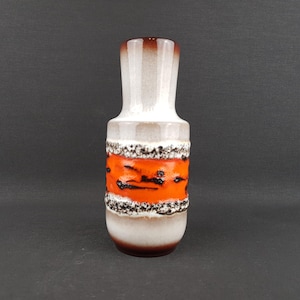 May include: A ceramic vase with a cylindrical shape, featuring a colour scheme of white, orange, and brown. The vase has a textured orange band with black accents, and a white and brown top and base. The vase is approximately 20 cm tall.