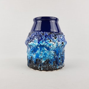 Puede incluir: Un jarrón de cerámica con un diseño texturizado y en capas en tonos azules y negros. La parte superior del jarrón es de un azul oscuro brillante y sólido, mientras que el cuerpo presenta una superficie rugosa y texturizada.