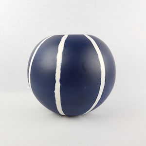 May include: A spherical navy blue vase with white vertical stripes. The ceramic vase has a smooth finish and a wide opening. This decorative piece is suitable for displaying flowers or as a standalone accent.