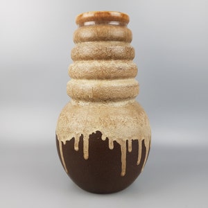 May include: A brown and beige ceramic vase with a textured, ribbed design. The vase has a rounded base and a narrow neck. The glaze is uneven, creating a drip effect.
