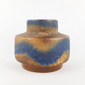 May include: A small, ceramic vase with a unique design. The vase features a cylindrical shape with a wide base and a narrower top. The exterior is a mix of brown, blue, and tan colors, creating a textured, earthy appearance. The vase is suitable for displaying small flowers or as a decorative piece.