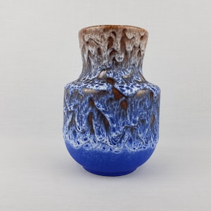 Puede incluir: Un jarrón de cerámica azul y marrón glaseado con un patrón ondulado. El jarrón mide aproximadamente 15 cm de alto y tiene un cuerpo redondo.