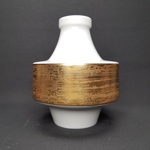 May include: White ceramic vase with a gold-toned band around the middle. The gold band has a textured, brushed look.