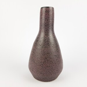 May include: A dark brown ceramic vase with a textured surface. The vase has a narrow neck and a wide, rounded base.