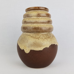 May include: A brown and cream ceramic vase with a textured, ribbed design. The vase has a rounded body and a slightly flared opening.