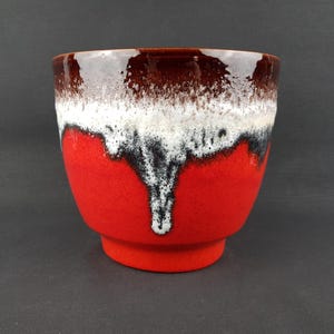 May include: A ceramic planter with a vibrant red base, transitioning to white and black accents, and a dark brown rim. The planter has a rounded shape and a small, circular base. The interior is dark brown.