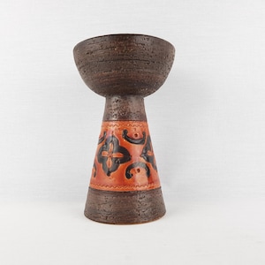 May include: A vintage ceramic vase with a textured, dark brown bowl-shaped top and a flared base. The base features a burnt orange band with black floral designs. A unique decorative piece.