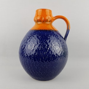 May include: A blue and orange ceramic vase with a textured surface and a handle. The vase is round and has a wide mouth.