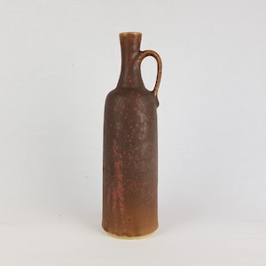 May include: A brown ceramic vase with a speckled glaze and a handle. The vase has a narrow neck and a wide base.