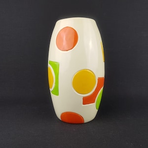 Könnte beinhalten: Eine cremefarbene Keramikvase mit einer abgerundeten ovalen Form. Die Vase ist mit großen, farbenfrohen Formen verziert: orange Kreise und Quadrate, gelbe Kreise und grüne Quadrate. Die Vase hat eine glänzende Oberfläche und eine glatte Textur.