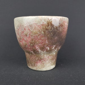 Könnte beinhalten: Eine handgefertigte Keramiktasse mit einer einzigartigen, strukturierten Oberfläche. Die Tasse hat eine Farbpalette aus Weiß, Rot und Braun mit einem Craquelé-Effekt. Sie hat eine breite Oberseite und einen schmaleren Boden, geeignet für Getränke.