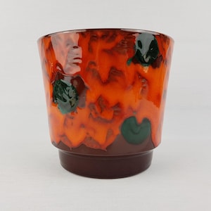 May include: A ceramic planter with a glossy, textured finish. The planter features a vibrant color palette of orange, brown, and green. The base is a solid brown, while the upper portion showcases an abstract design. A decorative piece for plants.