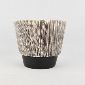 Op de afbeelding: Een keramische plantenbak met een textuur, verticaal gestreept ontwerp in crème en zwart. De plantenbak heeft een zwarte basis en een brede, licht uitlopende vorm. Ideaal voor kamerplanten.