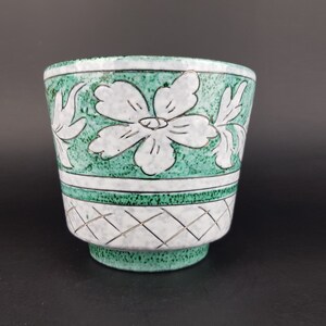 May include: A green ceramic planter with a white floral design. The planter has a textured surface and a wide, round opening.
