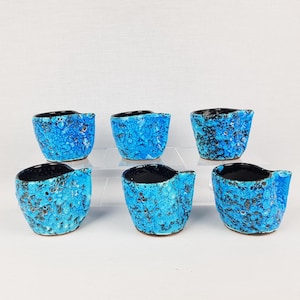 Puede incluir: Seis pequeñas tazas de cerámica azul y negra con una superficie texturizada. Las tazas están dispuestas en dos filas de tres.