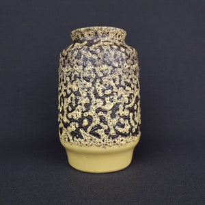 May include: A yellow ceramic vase with a brown speckled pattern. The vase has a rounded bottom and a wide opening.