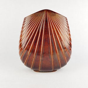 Pode incluir: Um vaso castanho, em estilo art déco, com um design em forma de leque. O vaso tem um acabamento brilhante e linhas verticais que irradiam do topo. A base é de um tom castanho mais escuro.