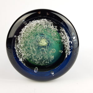 May include: A round glass paperweight with a dark blue rim and a green and white centre with air bubbles.