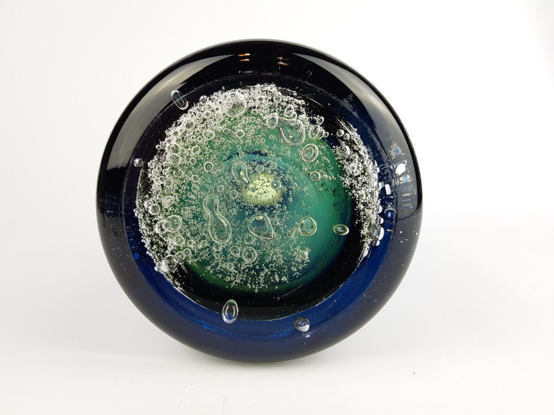 May include: A round glass paperweight with a dark blue rim and a green and white centre with air bubbles.