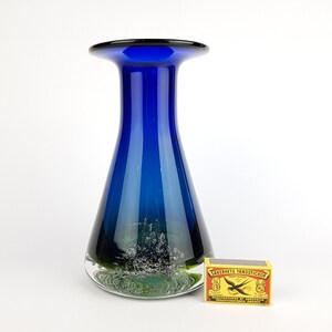 May include: A cobalt blue glass vase with a wide mouth and a rounded base. The vase has a textured, white and green design at the bottom.